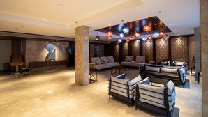 A spacious lobby with a modern design, featuring a large seating area with sofas and armchairs, a decorative wall with a globe, and a ceiling with hanging spherical lights. - Hotel Span International (Kanayannur)