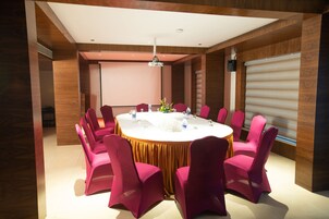 Un salón de conferencias con una mesa redonda, sillas rosadas y un mantel blanco.