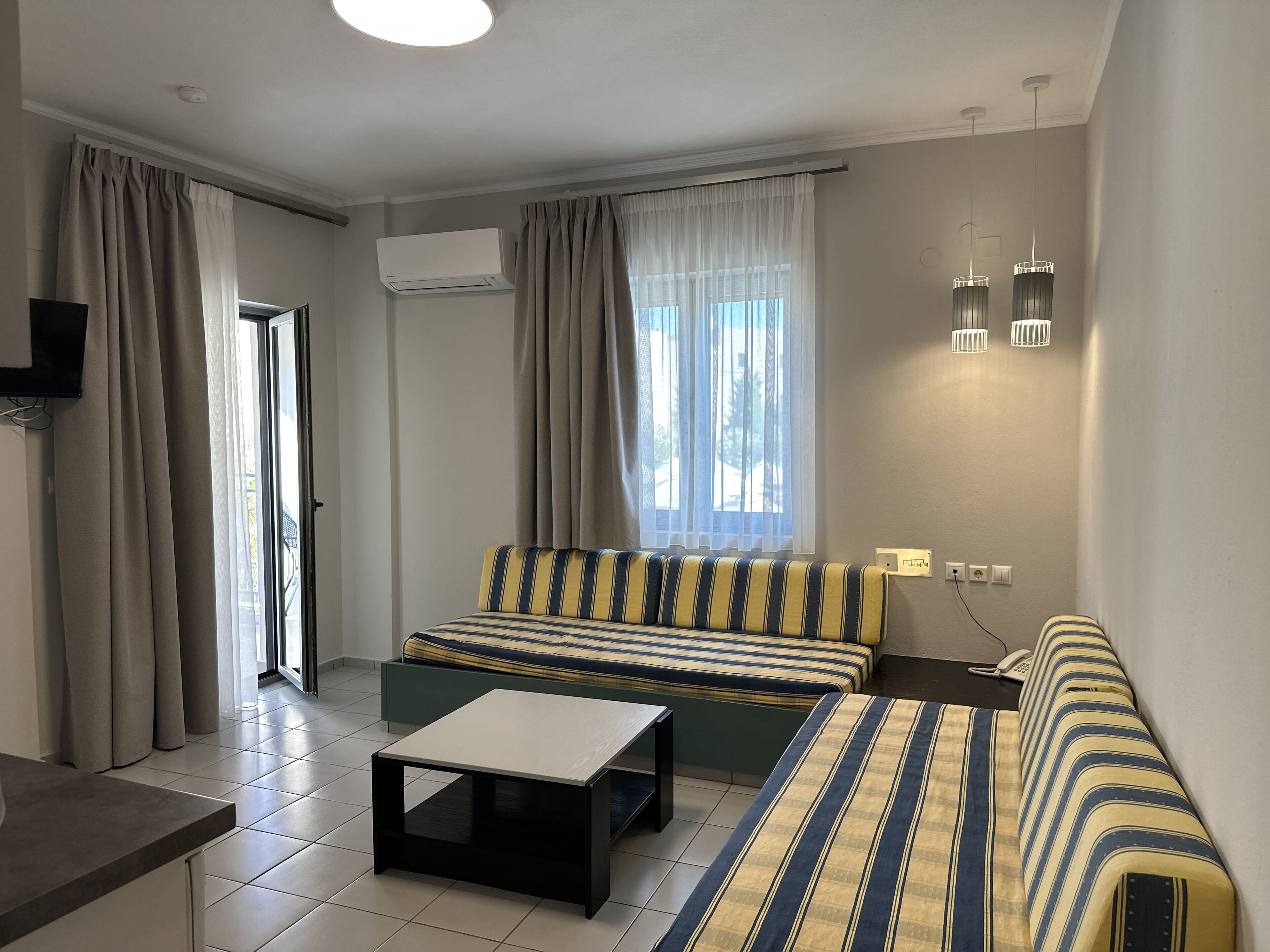 A modern hotel room with a sofa, a small table, a TV, and a window with curtains.