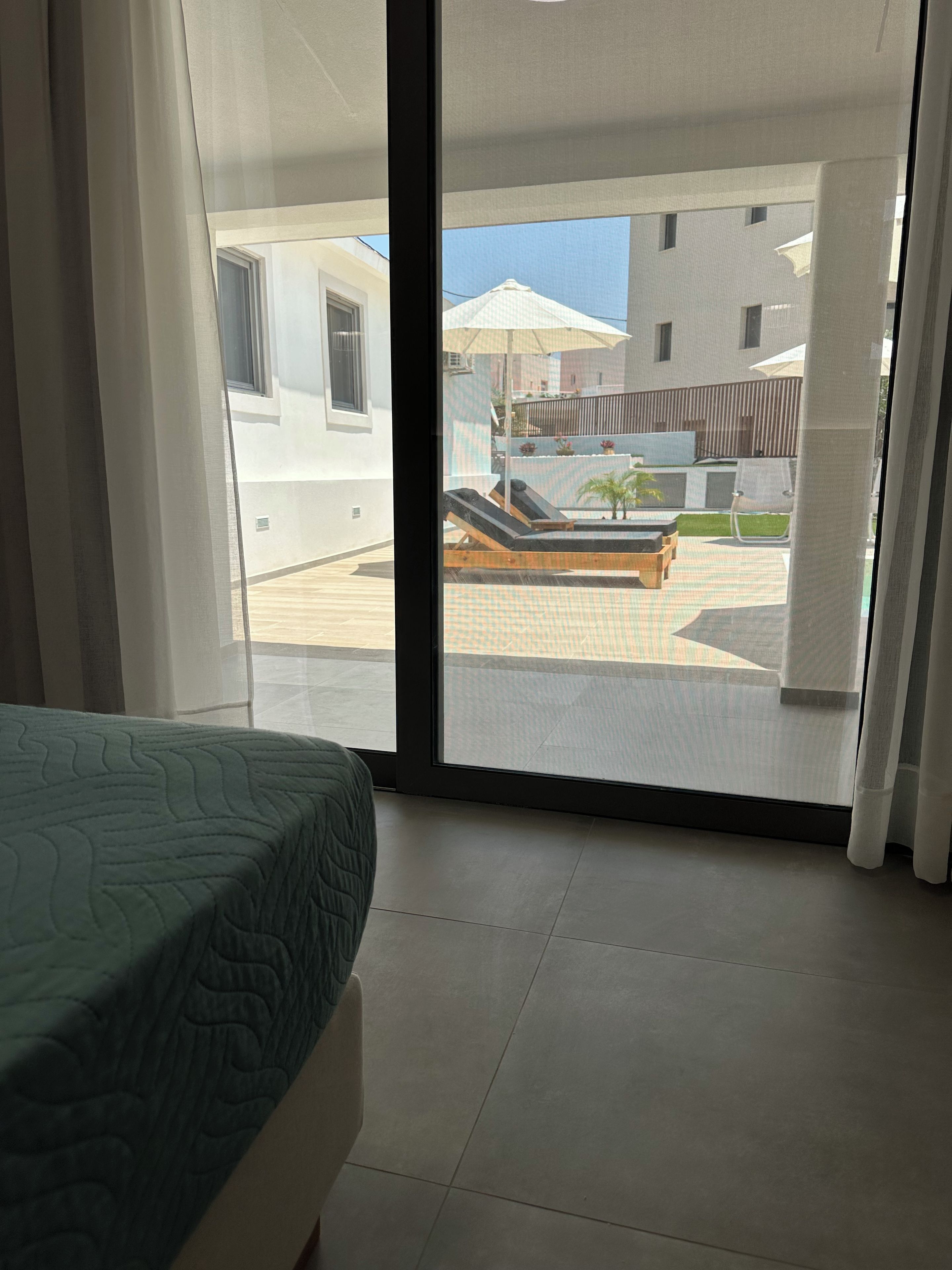 Une chambre dotée d’un lit et offrant une vue sur un espace extérieur comprenant une piscine, des chaises longues et des parasols.