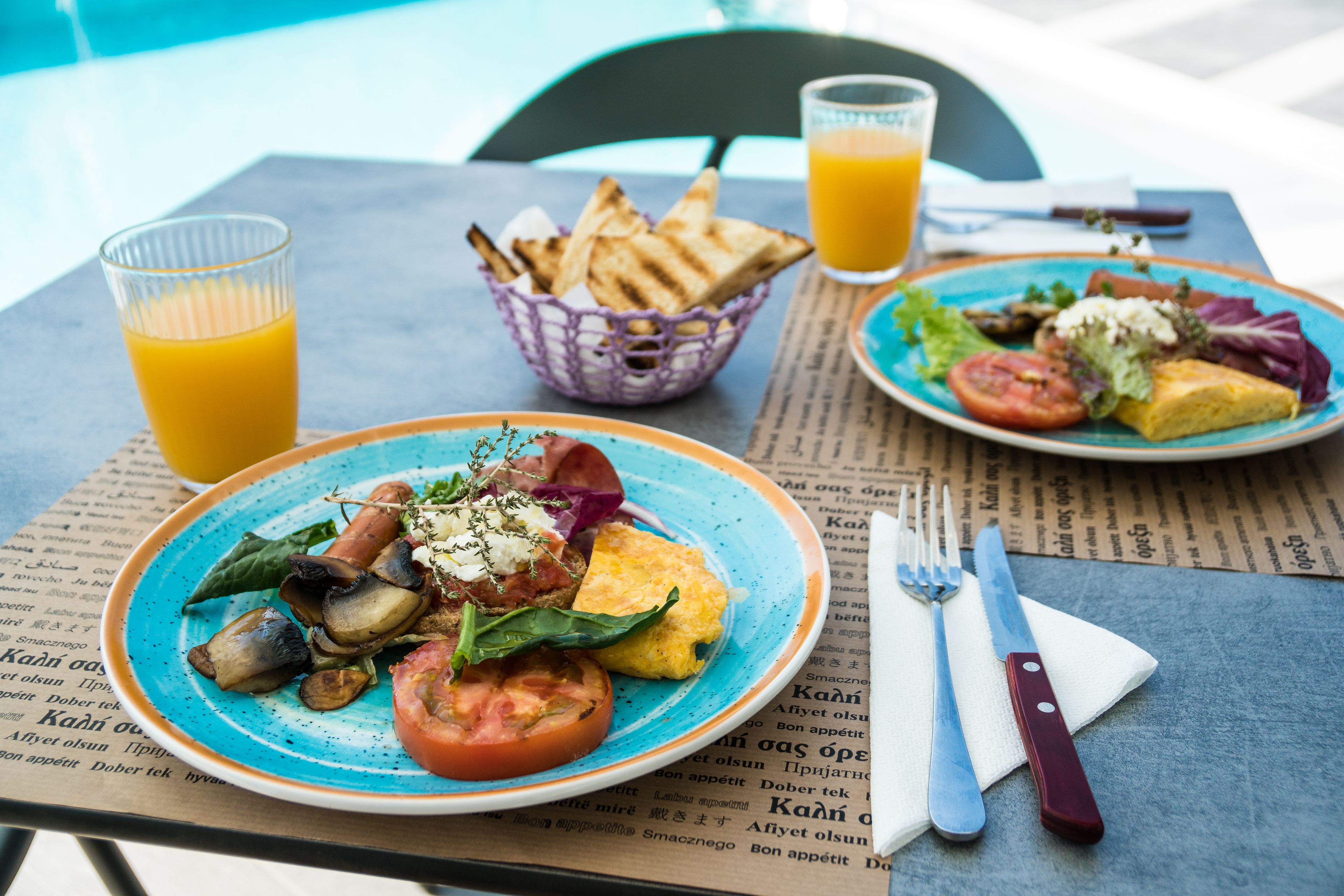 A table with plates of food, a basket of bread, and glasses of orange juice.