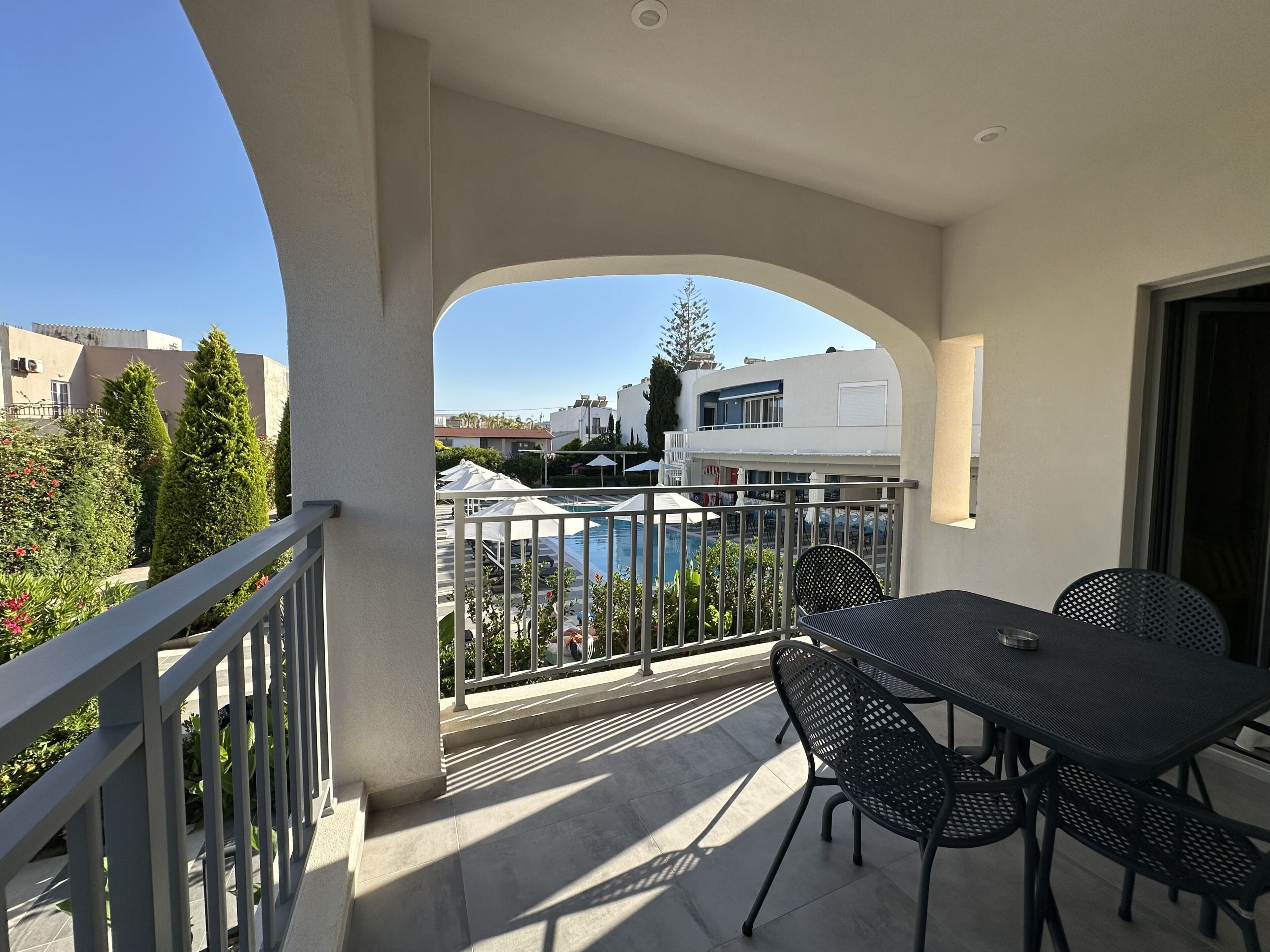 A balcony with a pool view, outdoor seating, and a clear sky.