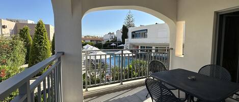A balcony with a pool view, outdoor seating, and a clear sky.