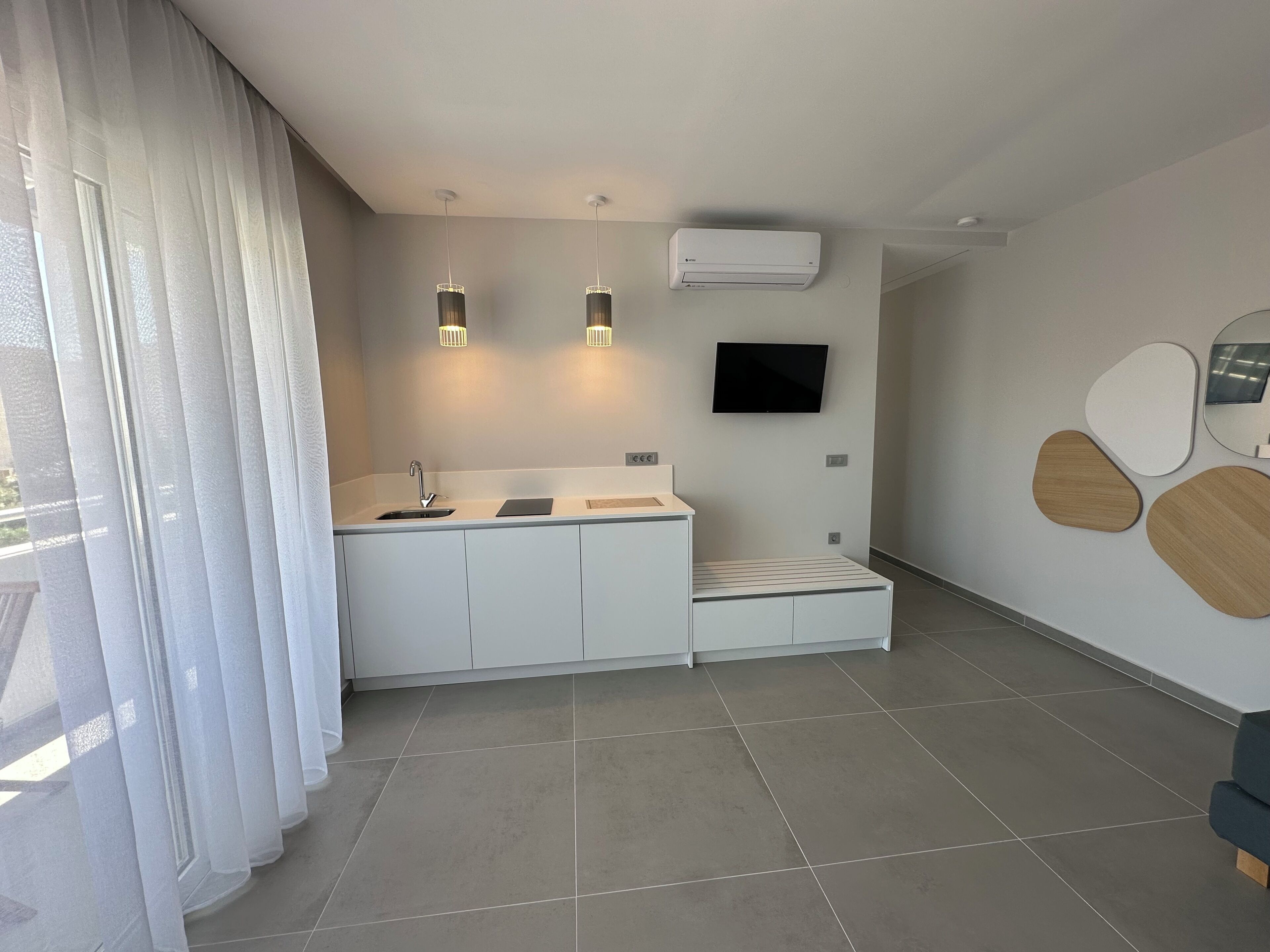 A modern kitchen with a built-in sink, two pendant lights, a flat-screen TV, and a minimalist design.