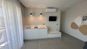 A modern kitchen with a built-in sink, two pendant lights, a flat-screen TV, and a minimalist design. - Evdokia Suites (Hersonissos)