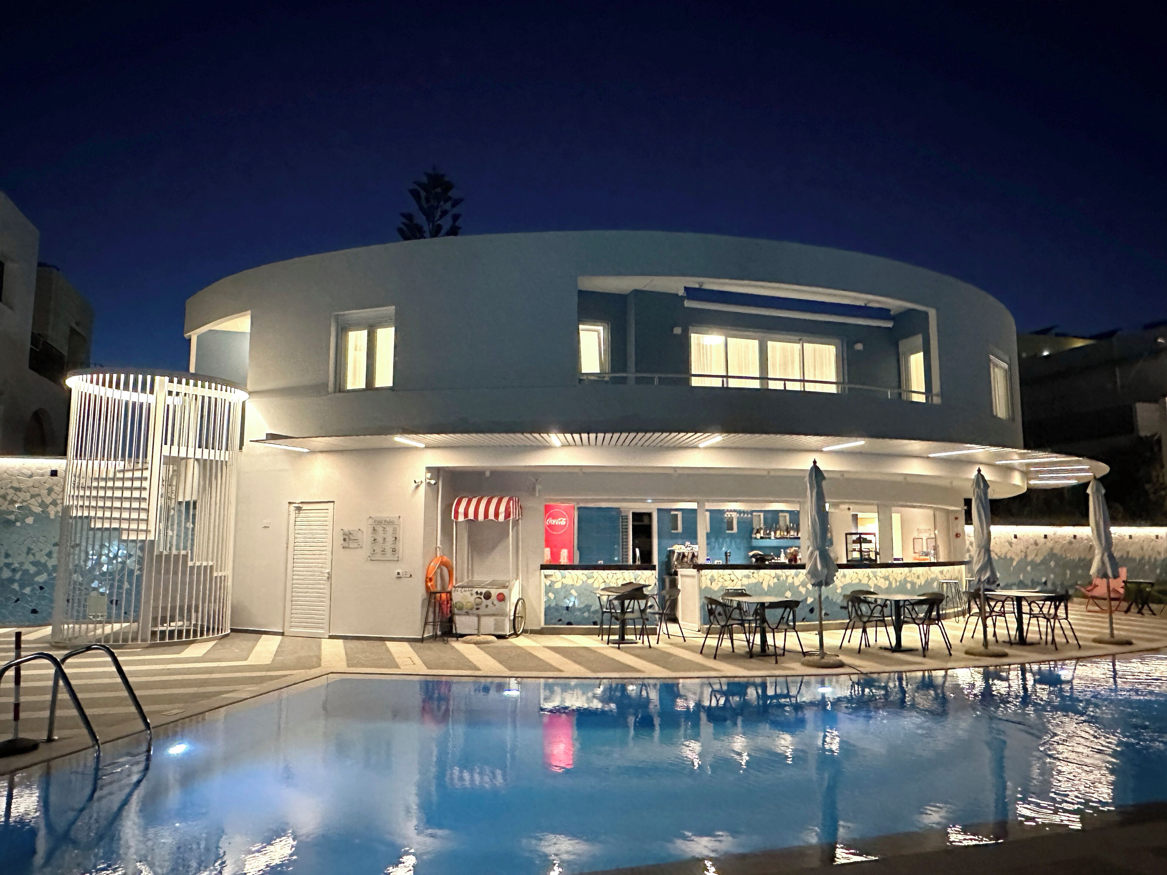 Un edificio moderno con piscina, asientos exteriores y un letrero de Coca-Cola.