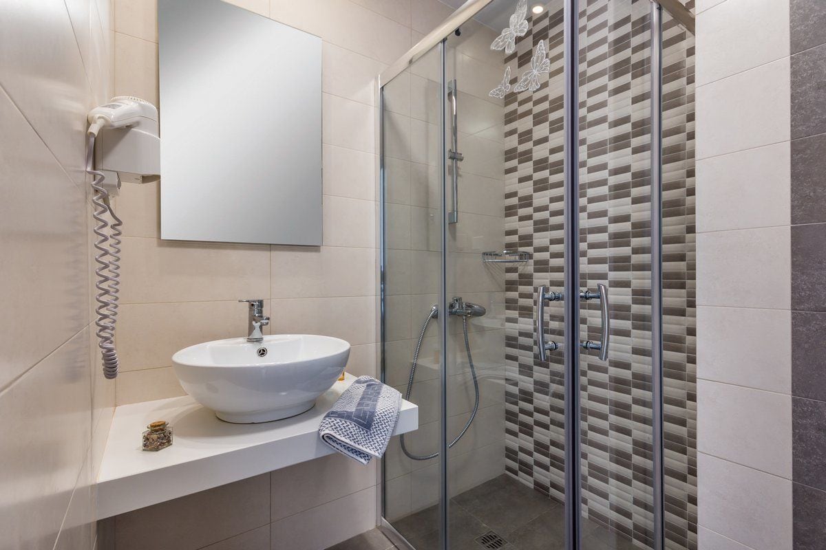 A modern bathroom with a white sink, a glass shower enclosure, and a tiled shower wall.