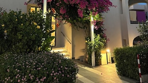 Un edificio moderno con fachada blanca, un acceso cubierto adornado con flores rosadas y una escalera que conduce a un nivel superior.