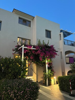 A modern building with a white facade, a covered entrance with pink flowers, and a staircase leading to an upper level. - Evdokia Suites (Hersonissos)