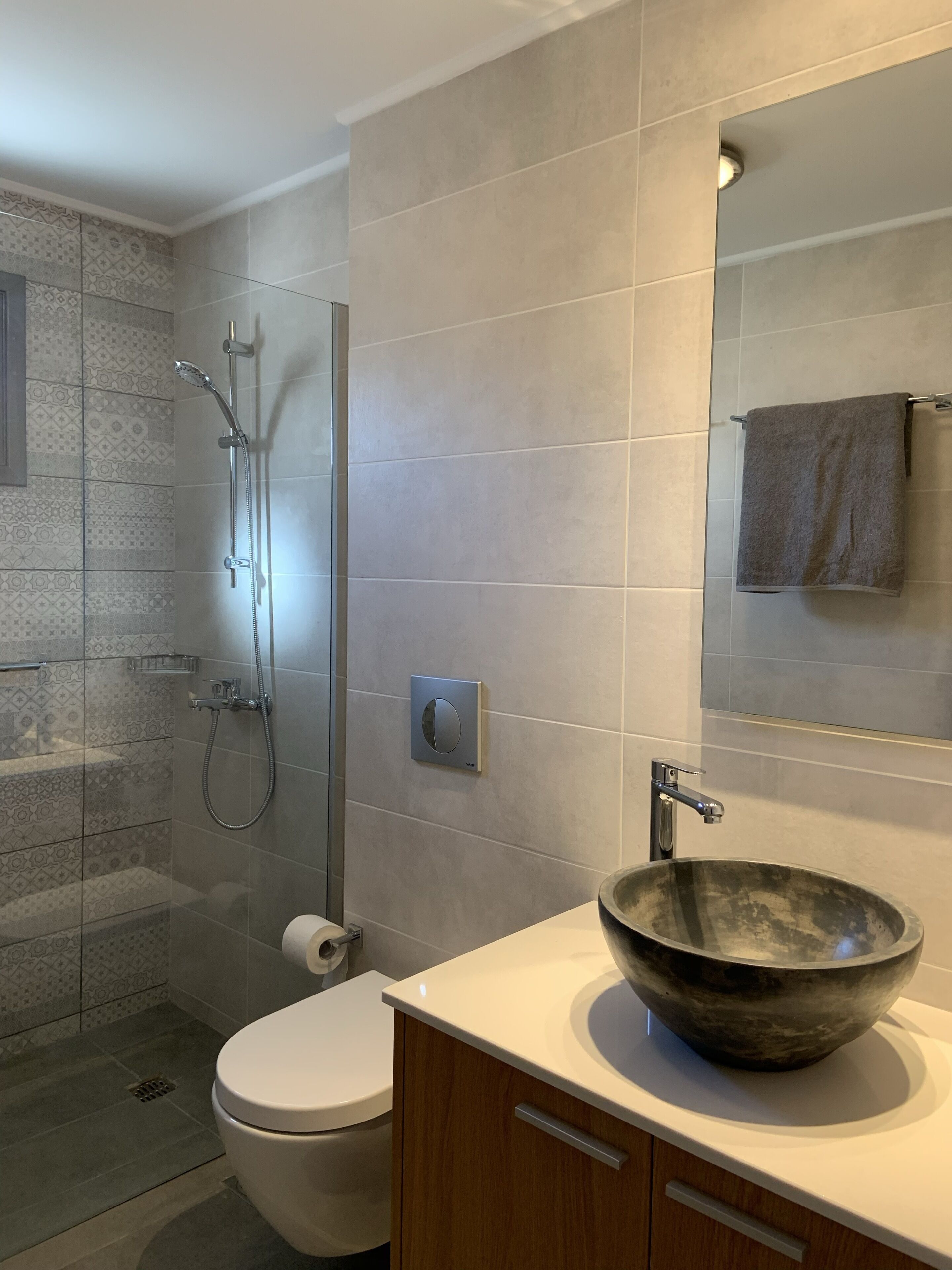 A modern bathroom with a glass shower enclosure, a toilet, a wooden cabinet, and a large mirror.