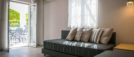 A modern bedroom with a sofa bed, a small wooden side table, and a large window with sheer curtains.
