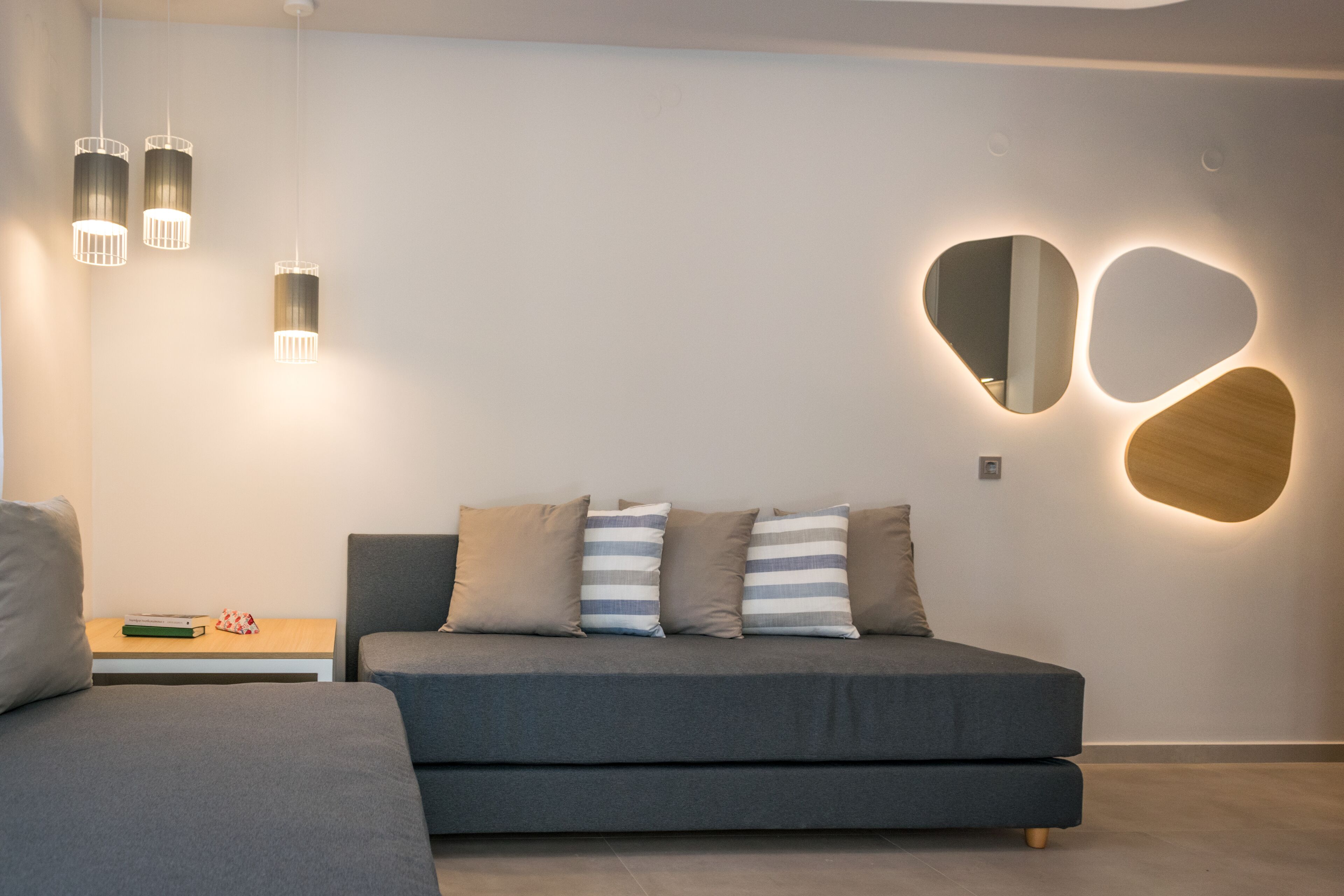 A modern bedroom with a grey sofa, a bedside table with books, and wall-mounted lighting.