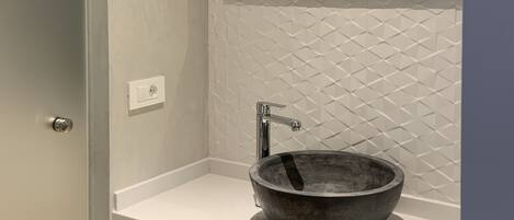 A bathroom with a white tiled wall, a large mirror, a round vessel sink, and a door.