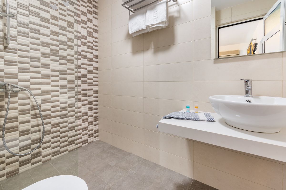 A modern bathroom with a checkered tile wall, a white sink, and a shower with a handheld showerhead.