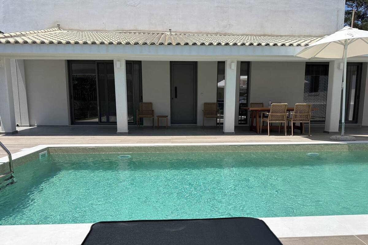 A pool area with a clear blue pool, a lounge chair, and a table with chairs.