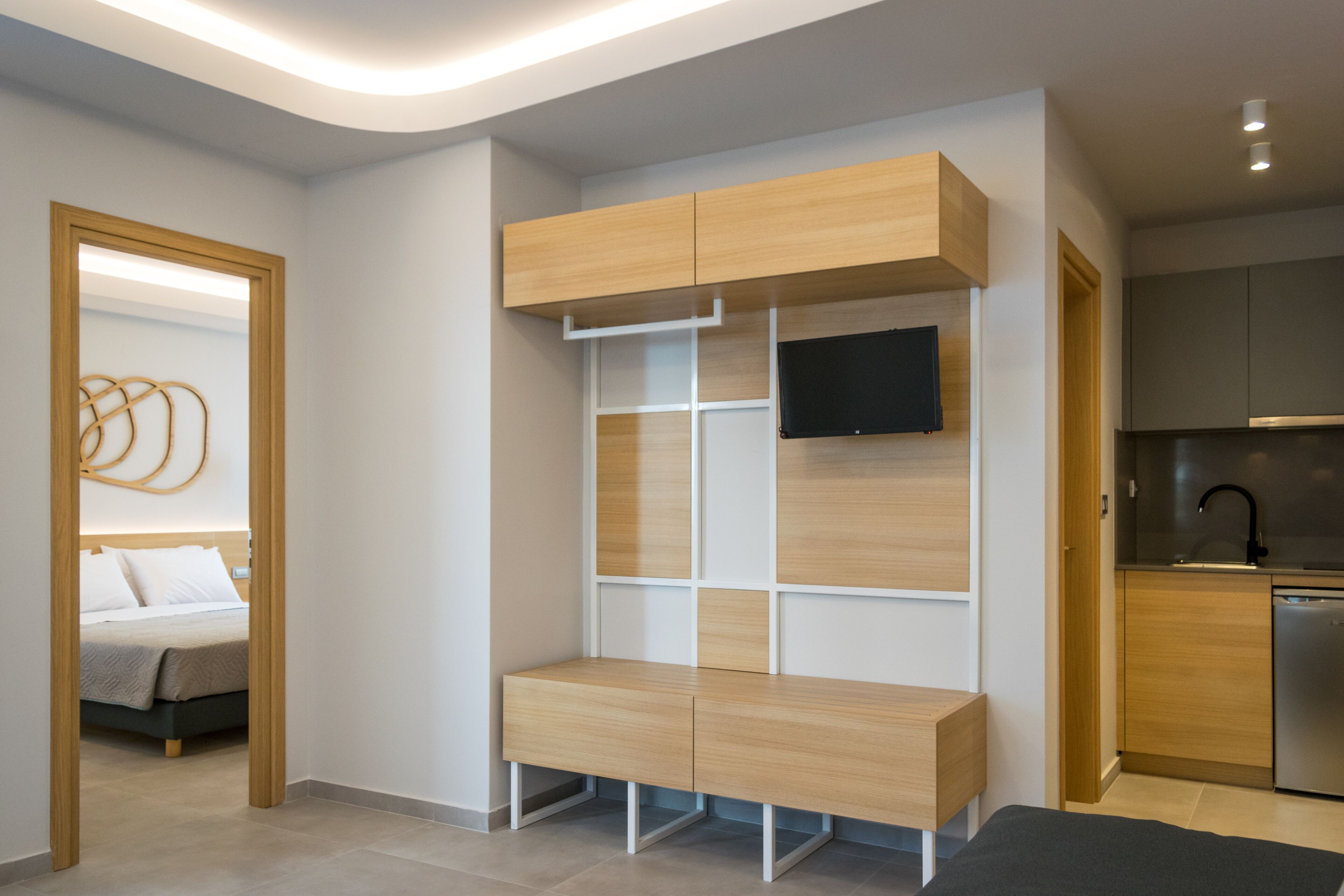 Een moderne slaapkamer met een ingebouwde bank, een aan de muur bevestigde televisie en een zichtbare keuken met een vaatwasser.