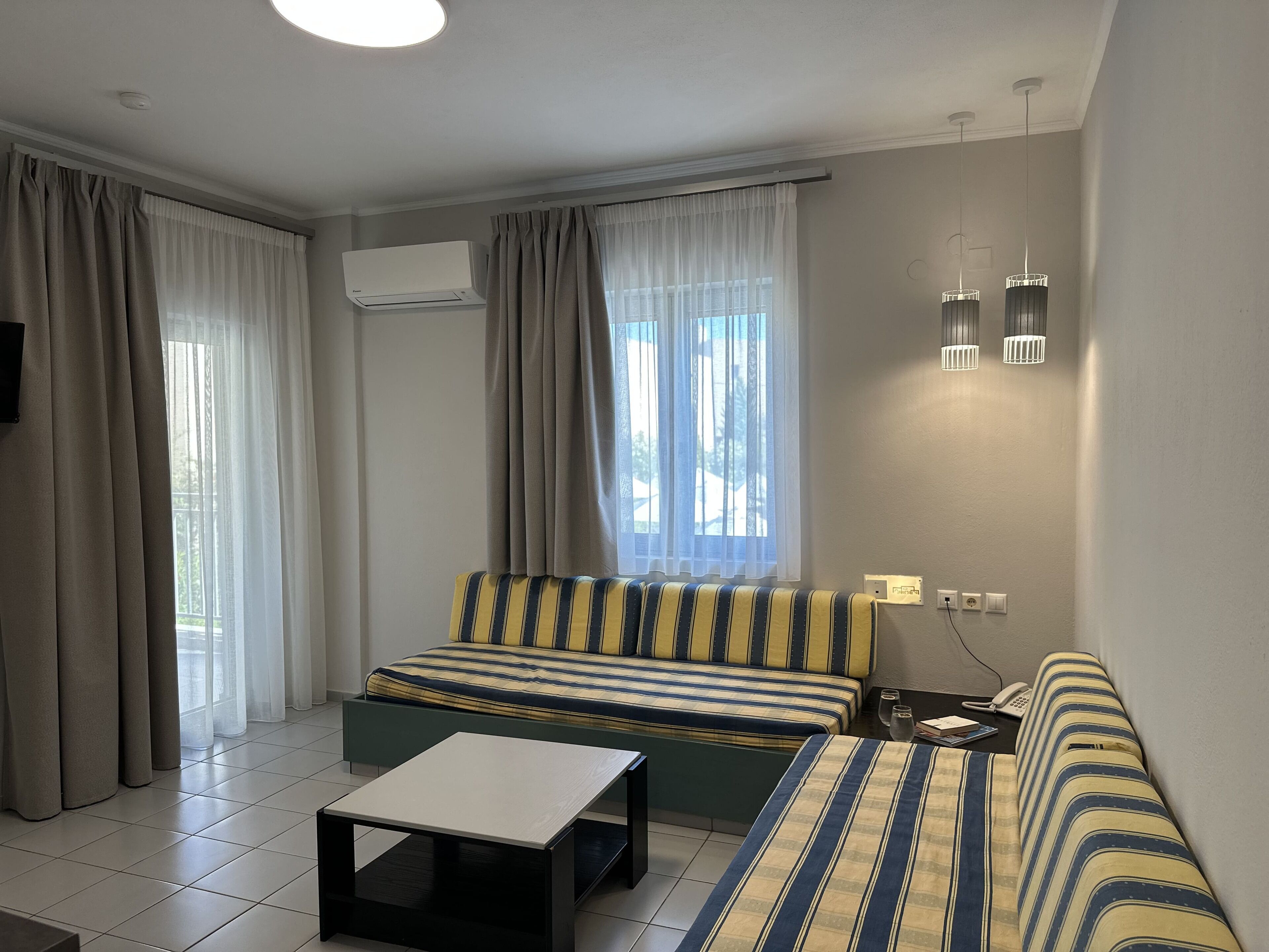 A modern hotel room with a sofa bed, a small table, a TV, and a window with curtains.