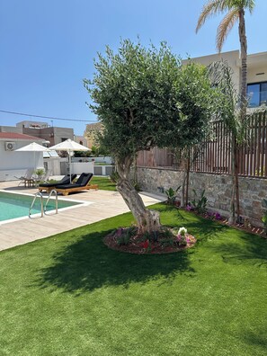 A swimming pool with lounge chairs, a tree, and a stone wall. - Evdokia Suites (Hersonissos)