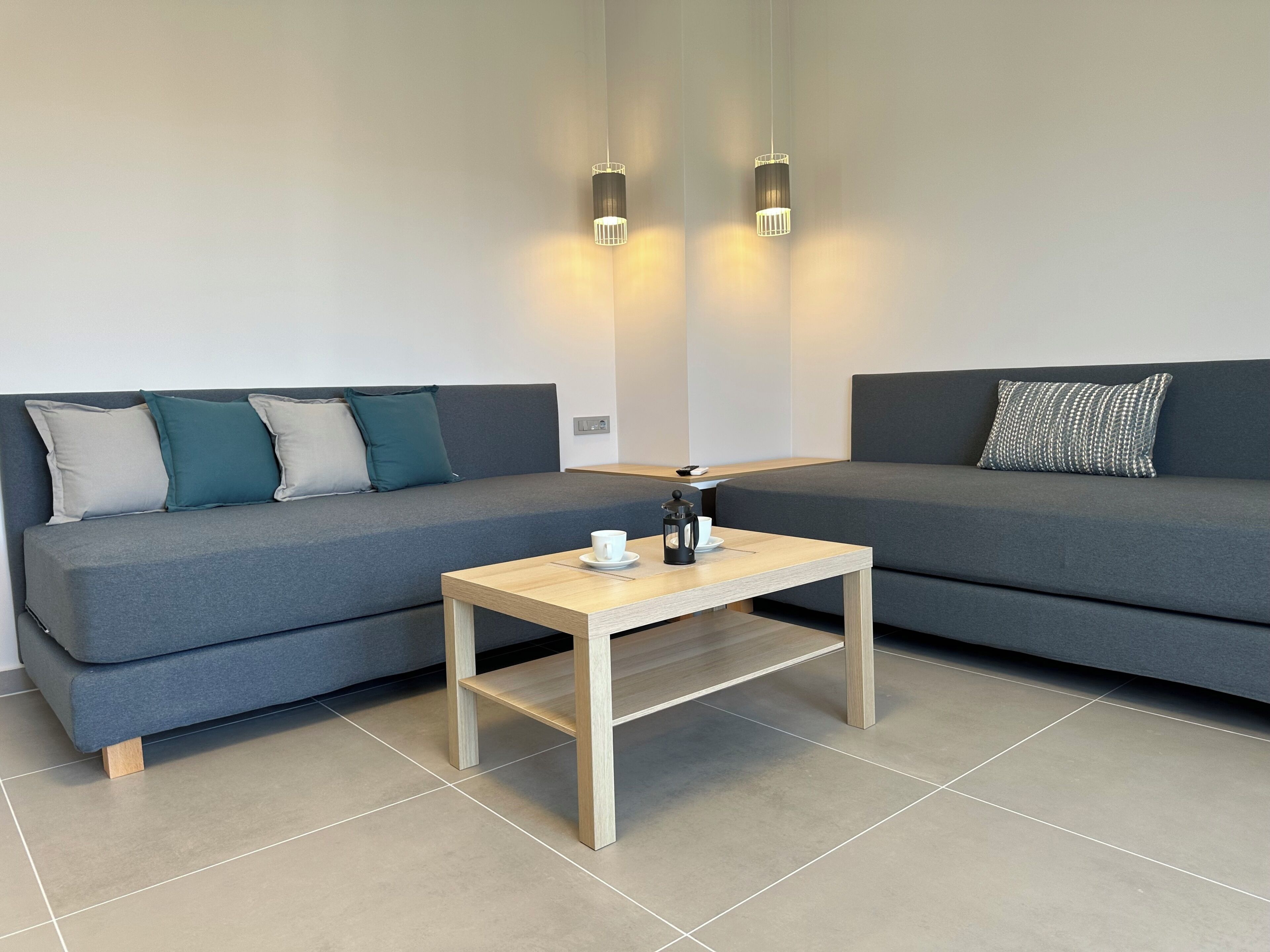 Ein modernes Wohnzimmer mit zwei grauen Sofas, einem Holztisch und zwei Pendelleuchten.