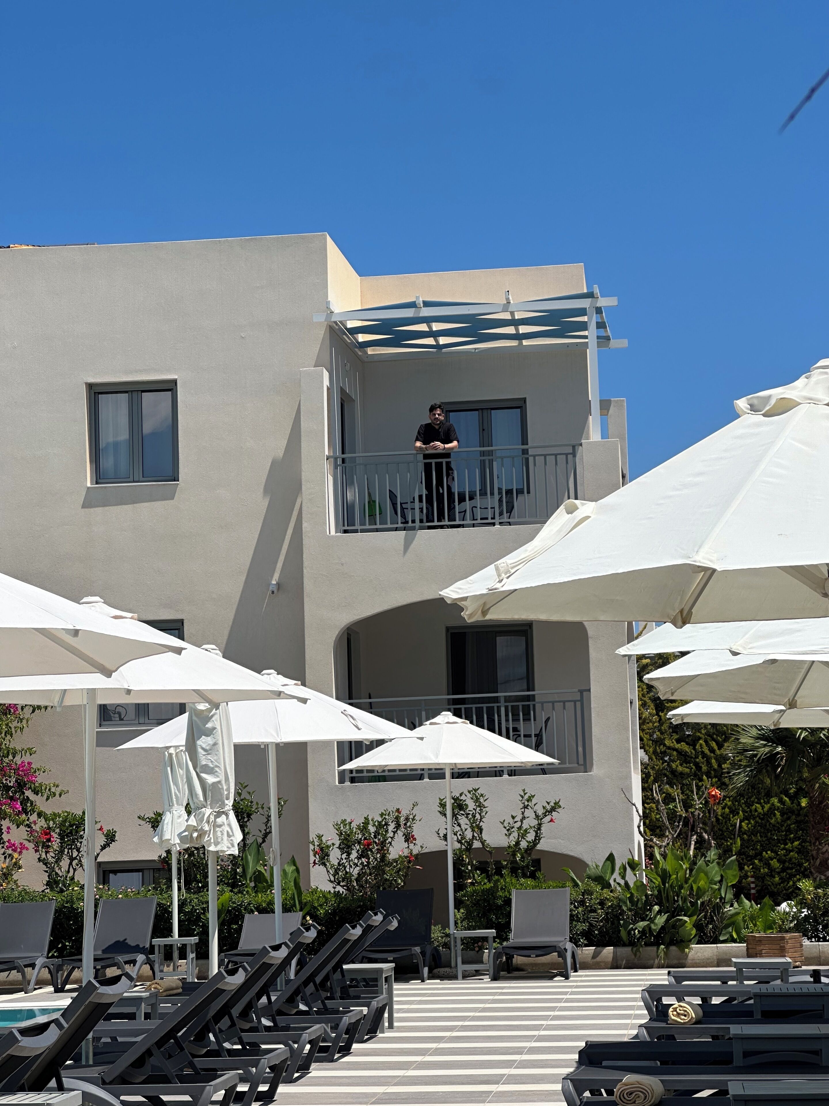 A hotel with a balcony, outdoor seating with umbrellas, and a pool area.