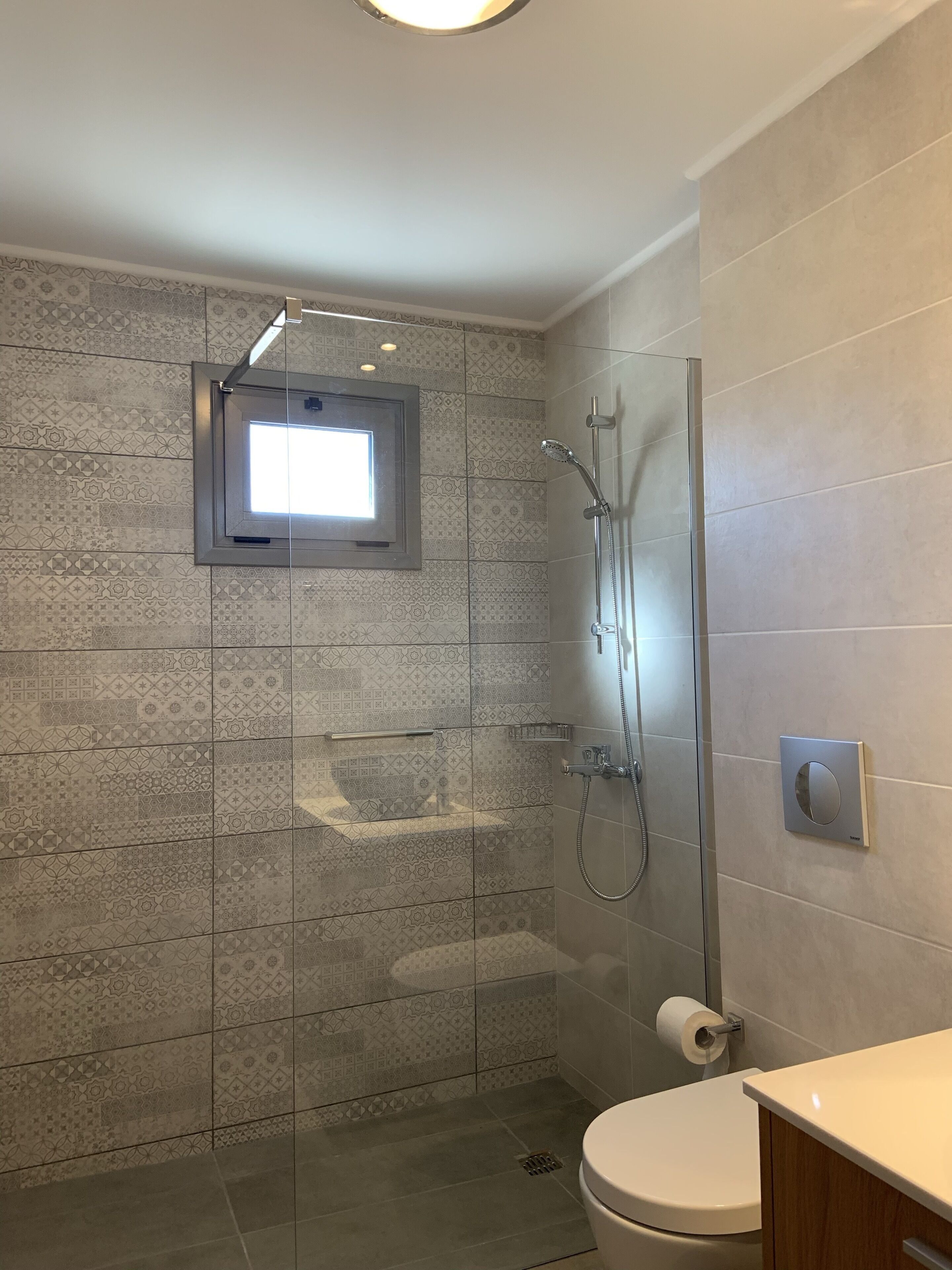 A modern bathroom with a glass-enclosed shower, a toilet, and a small window above the shower.