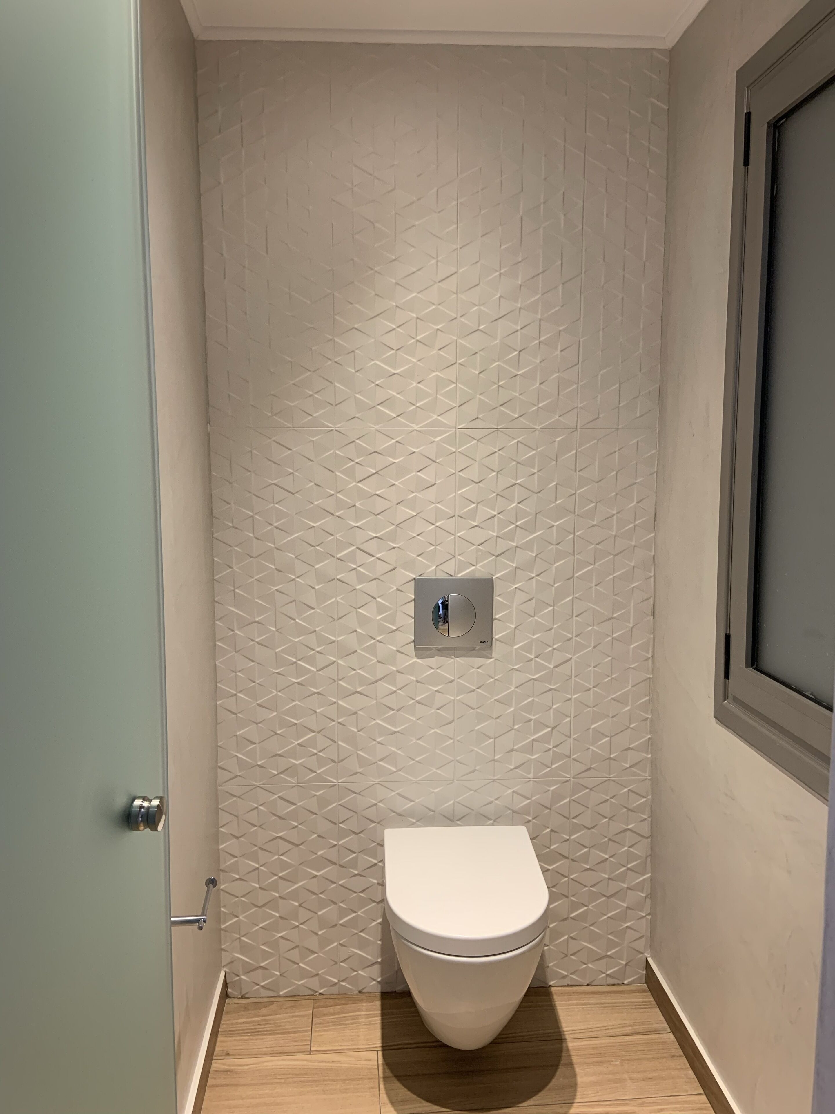 Une petite salle de bain moderne avec un mur orné d’un motif géométrique, des toilettes et un interrupteur.