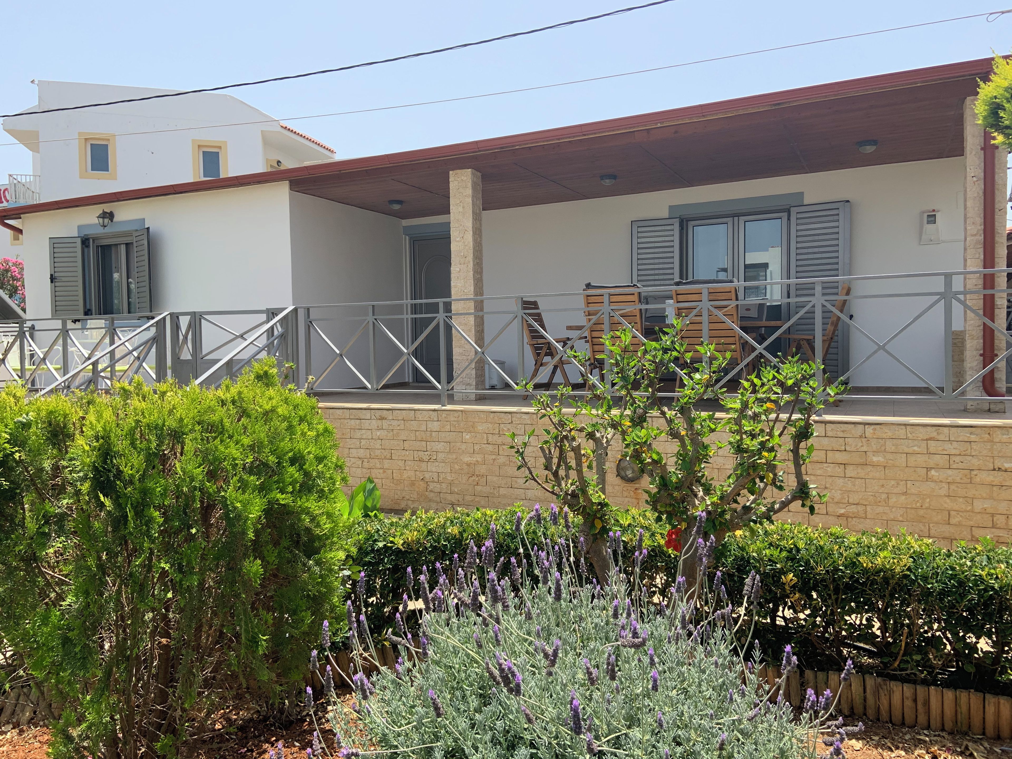A residential building with a covered porch, a brick wall, and a garden with lavender plants.
