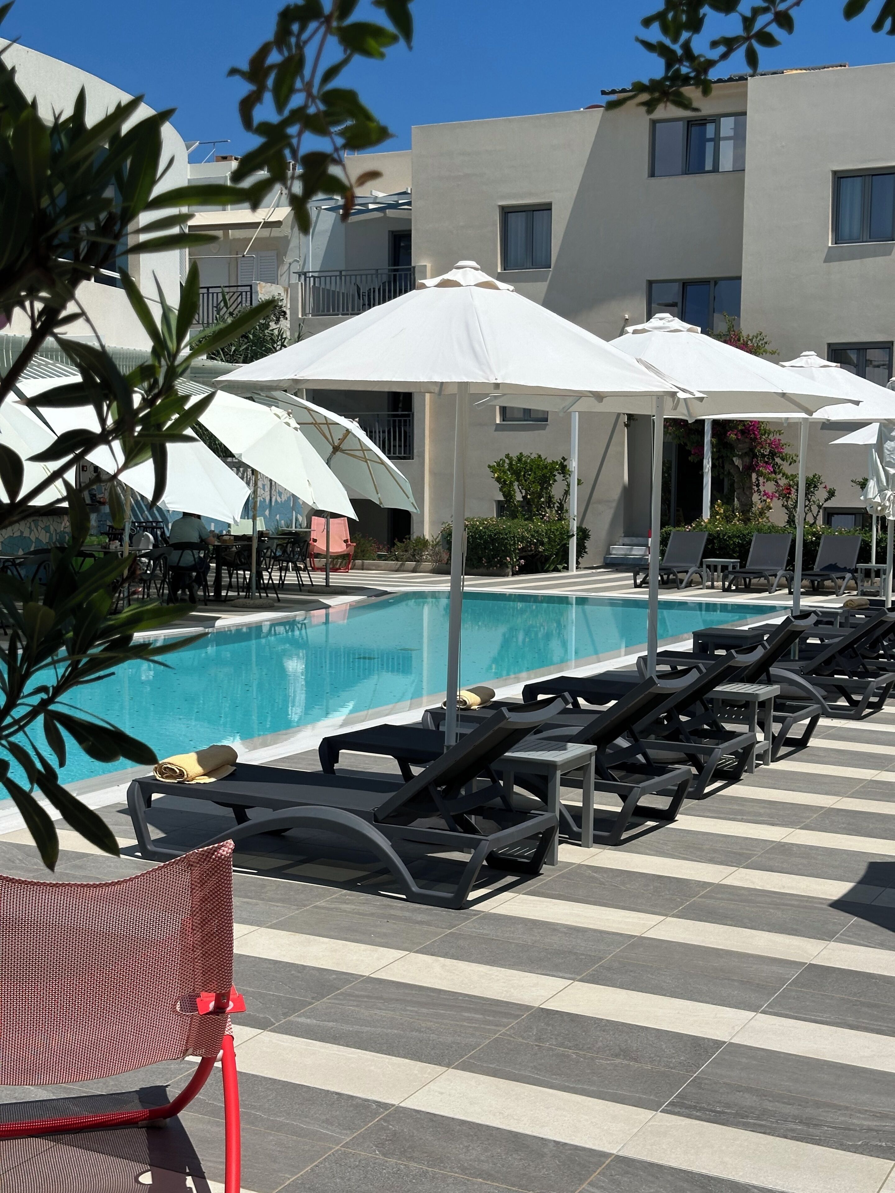 Un espace aménagé au bord de la piscine, avec des chaises longues, des parasols et une piscine.