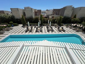 A pool area with lounge chairs and umbrellas, surrounded by buildings. - Evdokia Suites (Hersonissos)