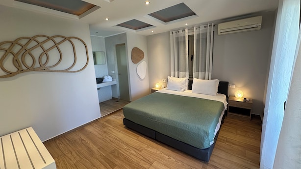 Un dormitorio moderno con una cama grande, suelo de madera, luces empotradas en el techo y un baño visible al fondo.
