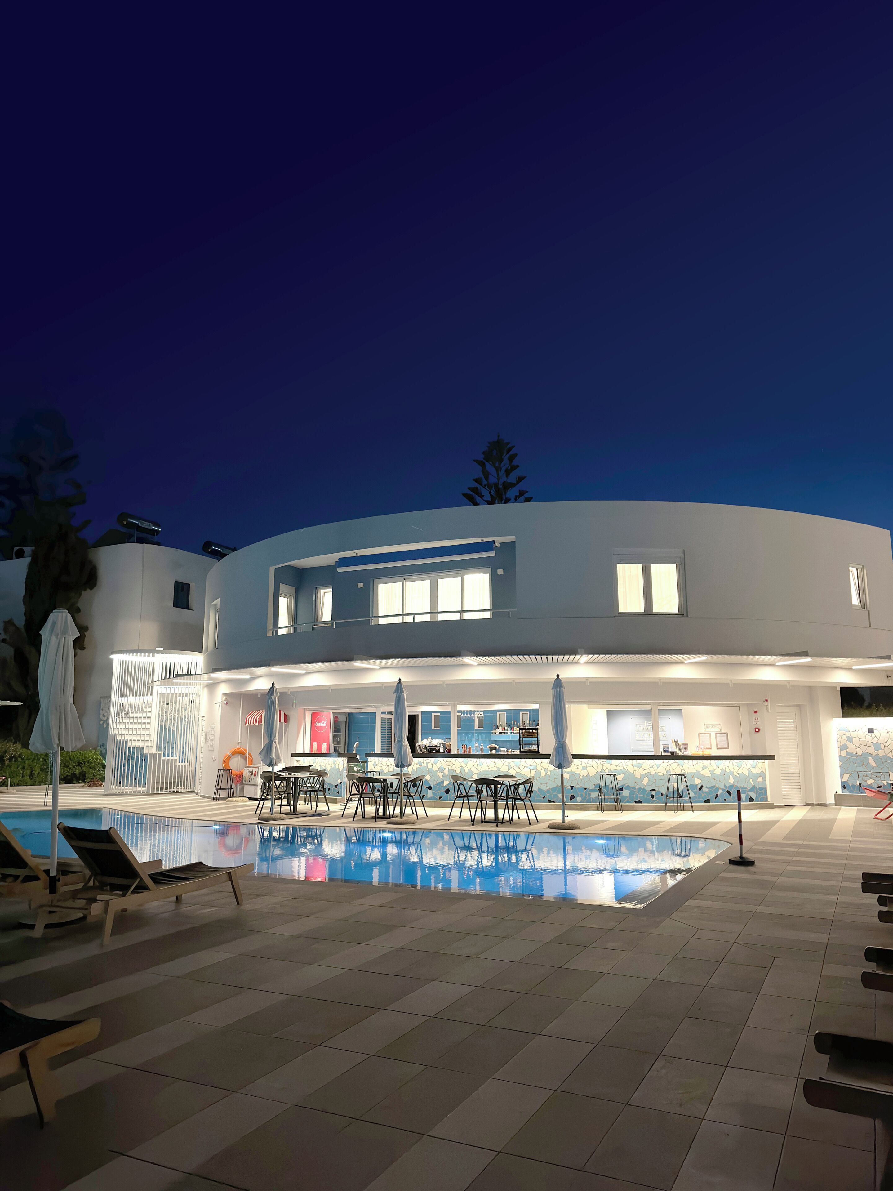 A modern hotel with a swimming pool, outdoor seating, and a bar area.
