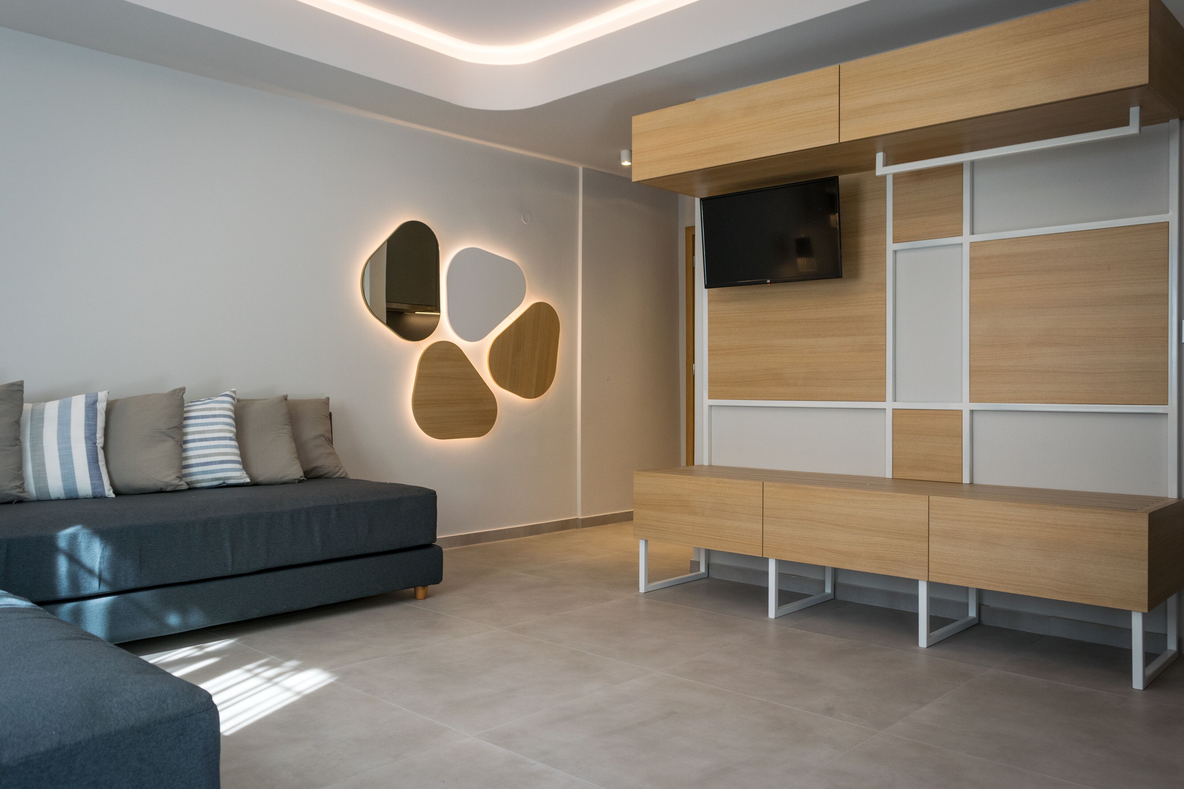 Un salon moderne avec un canapé, un téléviseur fixé sur un meuble en bois et un mur agrémenté d’un luminaire au design géométrique.