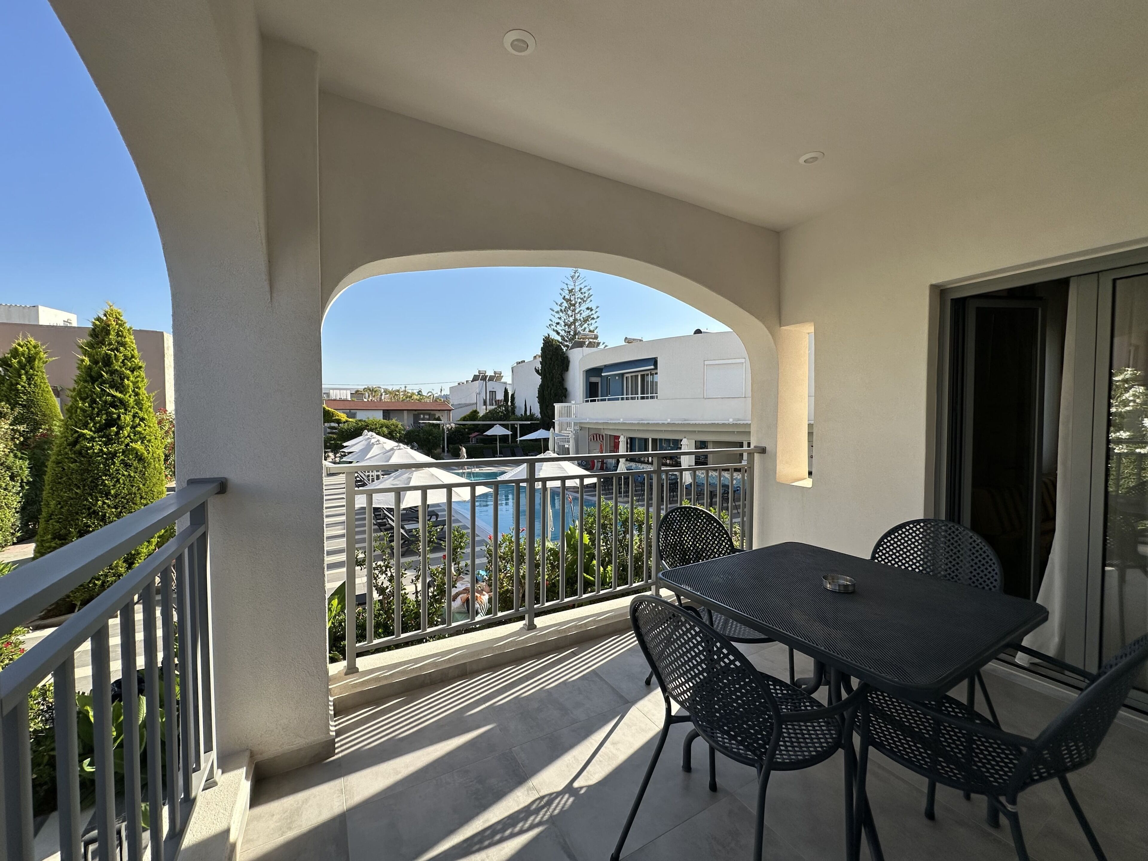 A balcony with a table and chairs, overlooking a swimming pool and buildings.