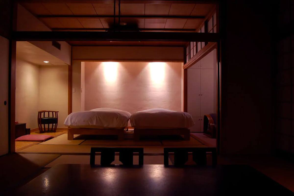 A traditional Japanese room with tatami flooring, two low beds, a wooden bench, and a sliding door.