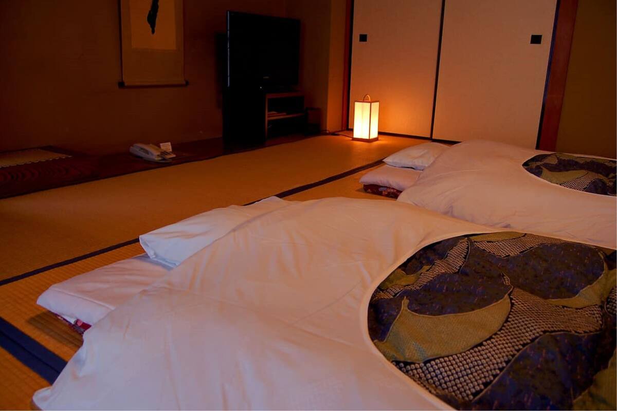 A hotel room with two beds, a television, and a traditional Japanese lantern.