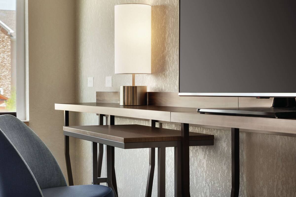 A modern hotel room with a flat-screen TV, a bedside table with a lamp, and a chair.