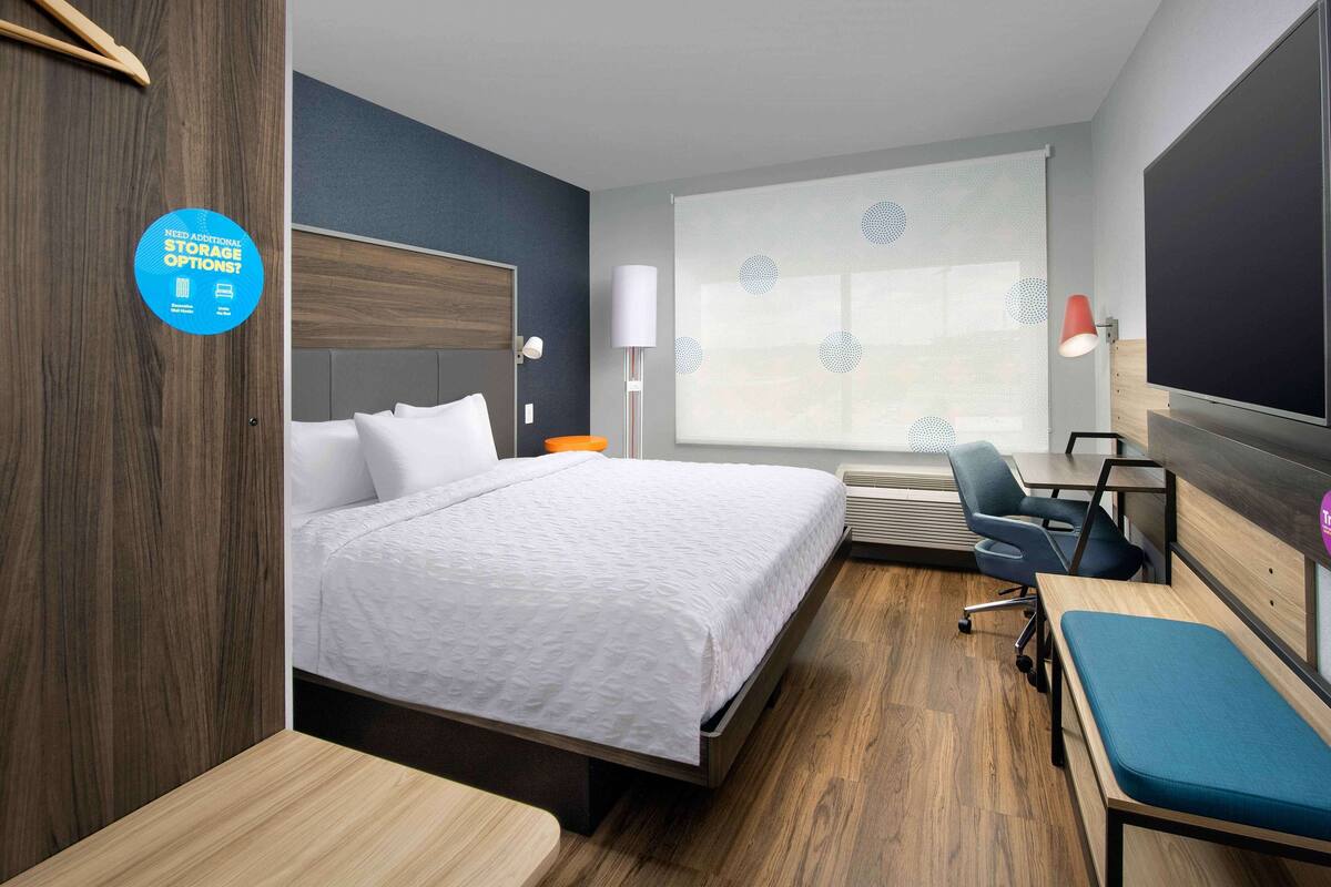 A hotel room with a bed, a desk, a chair, a TV, and a window with a view.