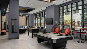 Un espacio recreativo moderno en el interior, con mesas de billar, asientos cómodos y ventanas amplias.
