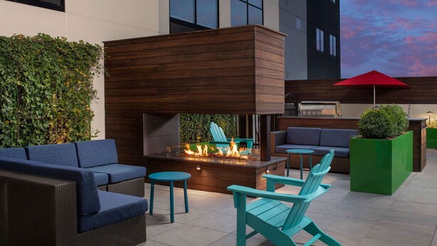Un espacio moderno para sentarse al aire libre con un brasero, mobiliario azul y una maceta verde.