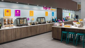 Un área de desayuno moderna con una barra que exhibe diferentes alimentos y un letrero que dice "TOP IT BREAKFAST".