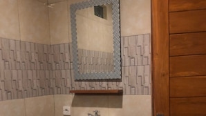 A bathroom with a white sink, a mirror with a geometric pattern, and a wooden door. - Cantika Guest House (Pecatu)