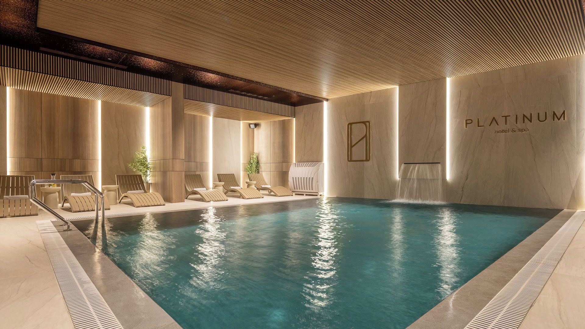 Piscina interior moderna con sillones de descanso y una cascada.
