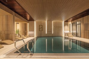 En modern inomhuspool med träinredning, en glasvägg och en skylt med texten ”PLATINUM hotel & spa”.