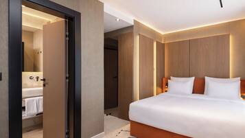 A modern hotel room with a large bed, a walk-in closet, and a bathroom with a visible sink and towel rack.