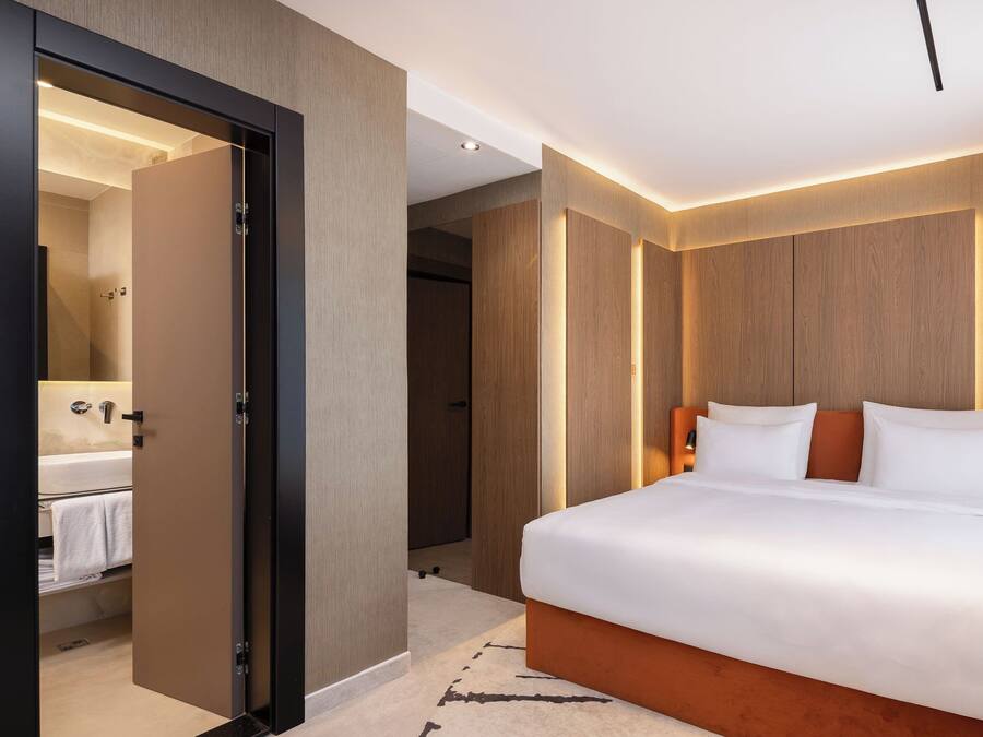 A modern hotel room with a large bed, a walk-in closet, and a bathroom with a visible sink and towel rack.