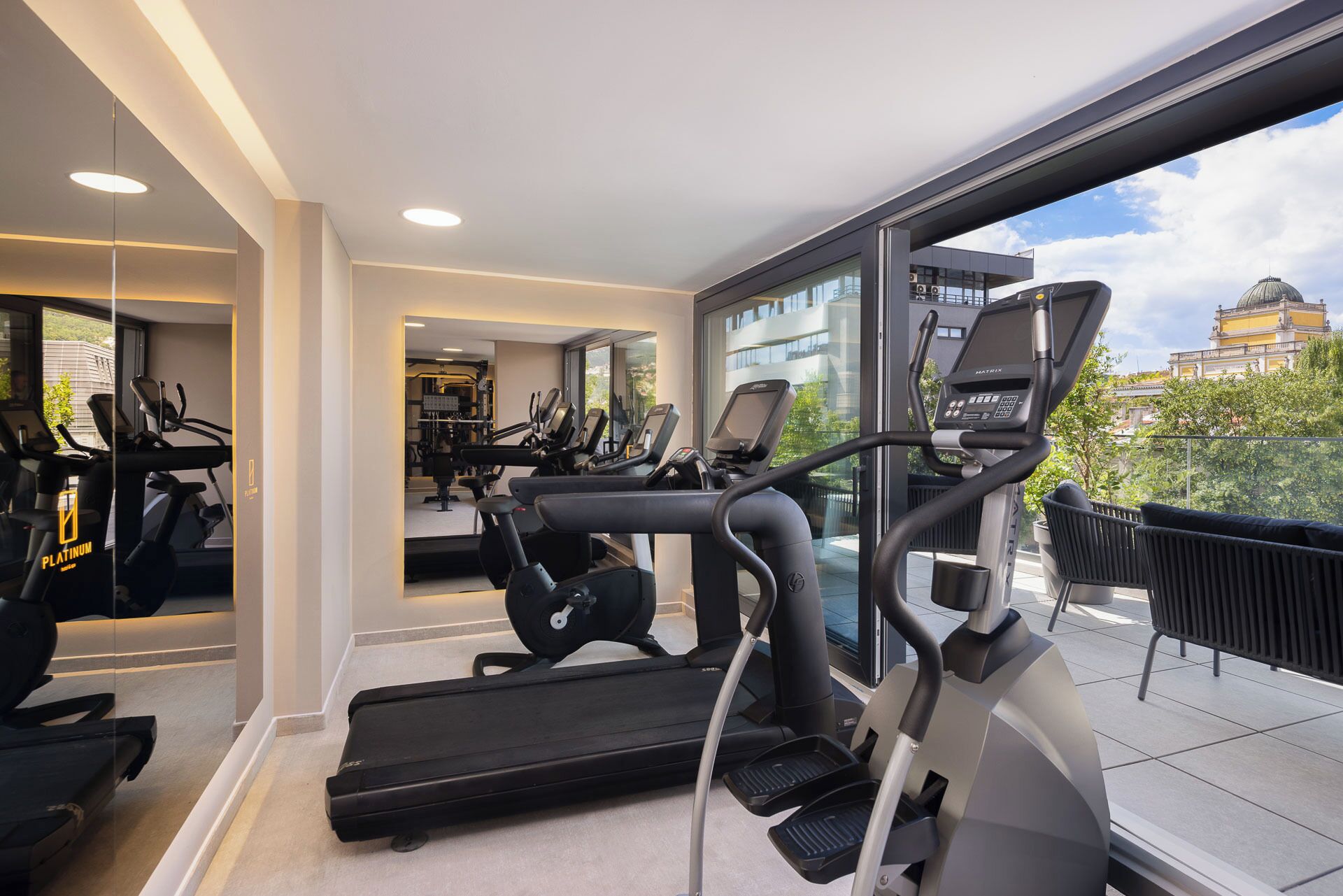 Une salle de sport moderne équipée de tapis de course, de vélos d’appartement et d’un mur entièrement recouvert de miroirs.