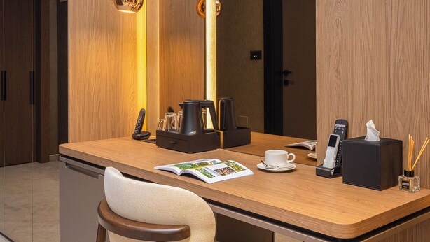 A modern hotel room with a wooden desk, a chair, a large mirror, and a minibar. - PLATINUM hotel & spa (Sarajevo)