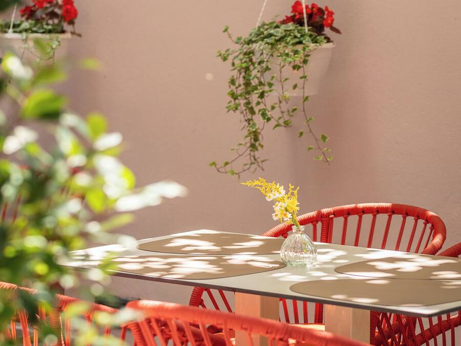 A round table with a glass vase, surrounded by red chairs, and hanging planters with red flowers.