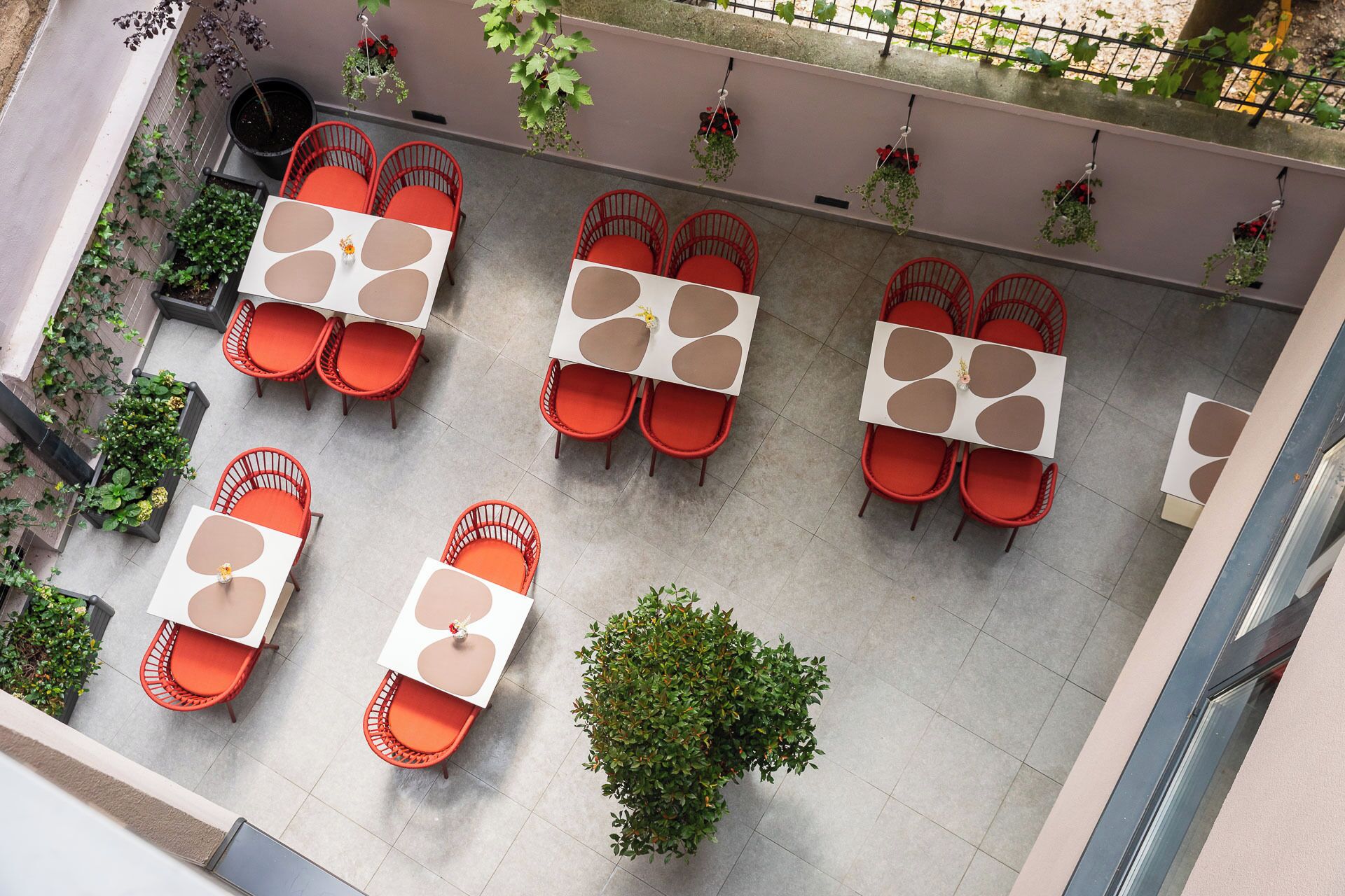 An outdoor seating area with tables and chairs, surrounded by potted plants and a metal fence.