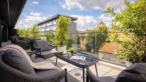 A balcony with outdoor furniture, a glass table, and a view of buildings and trees. - PLATINUM hotel & spa (Sarajevo)